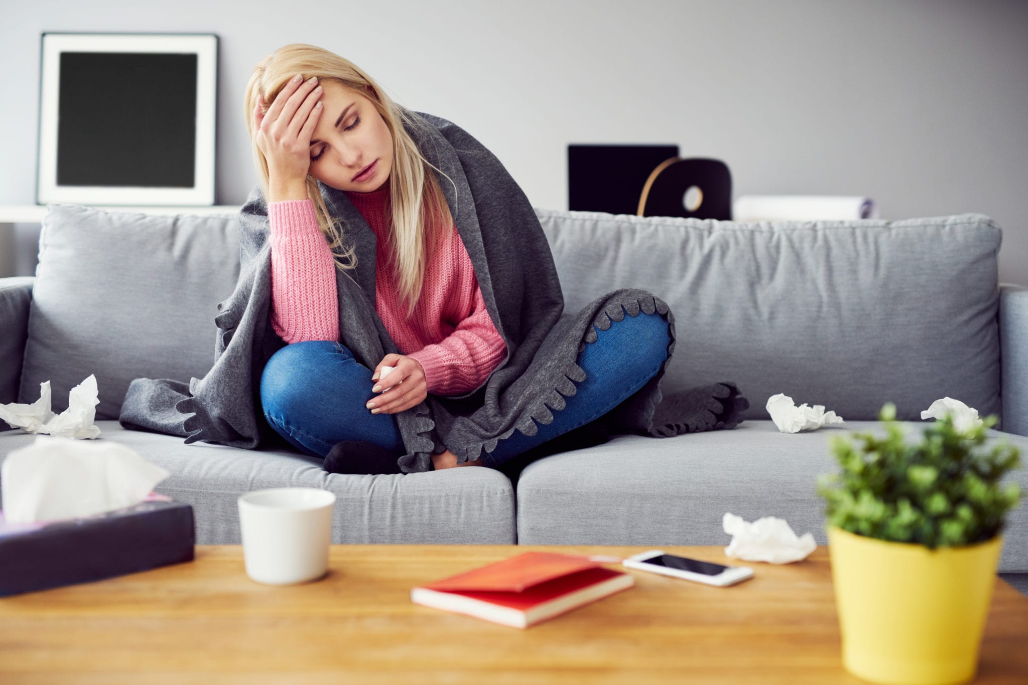 Sick woman with headache sitting under the blanket in living room